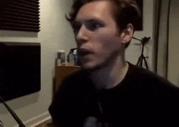 a young man in a black shirt is standing in a room with a microphone .