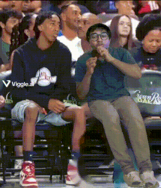 two men are sitting in the stands at a basketball game and one of them is wearing a crown royale sweatshirt
