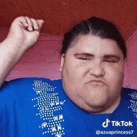 a woman in a blue shirt is making a funny face with her fist up .