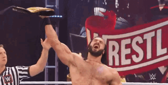 a wrestler holds up his championship belt in front of a wrestl banner