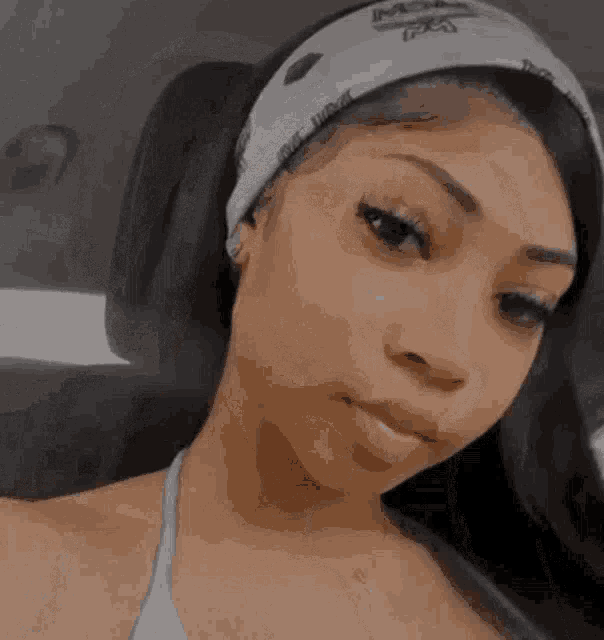 a woman wearing a headband and a white tank top is sitting in a car .
