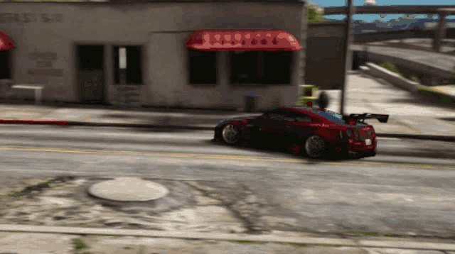 a red car is driving down a street in front of a building that says ' a & a ' on the side
