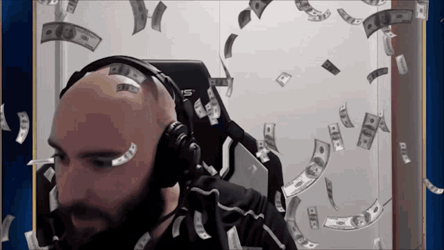 a bald man wearing headphones is surrounded by hundred dollar bills that are falling from the sky