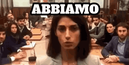 a woman stands in front of a group of people with the word abbiamo above her head