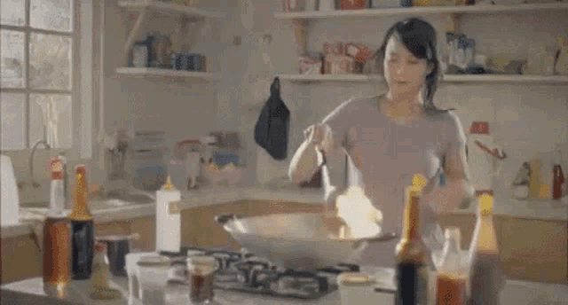 a woman is cooking food in a frying pan that is on fire in a kitchen .