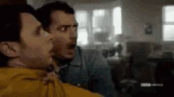 two men are standing next to each other in a living room and one of them is holding the other 's neck .