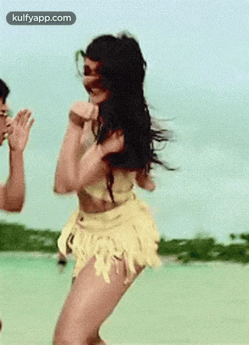 a woman in a yellow skirt is dancing on the beach while a man watches .