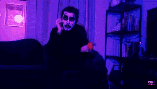 a man in a joker costume is sitting on a couch talking on a cell phone .