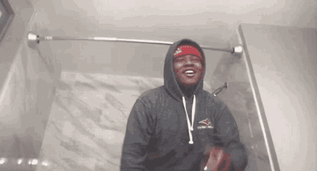 a man in a hoodie and headband is sitting in a shower .
