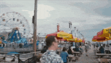 a man walking down a boardwalk with a ferris wheel in the back