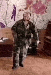 a man in a military uniform is dancing in a living room with flowers on the wall .