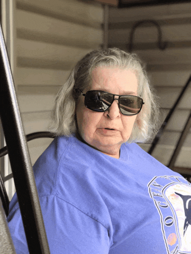 an older woman wearing sunglasses and a blue shirt that says ' apollo ' on it