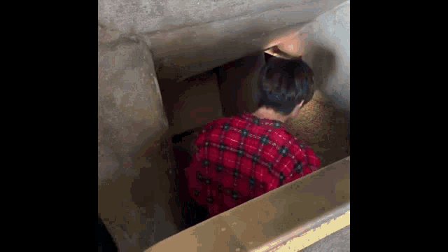 a man in a red plaid shirt is standing in a narrow tunnel .