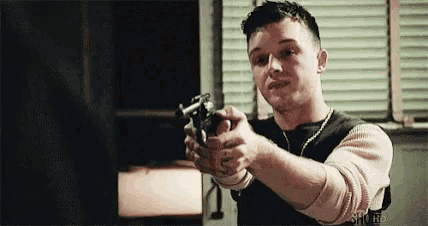 a man is holding a gun in his right hand and pointing it at the camera .