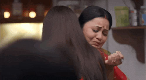 two women are sitting next to each other in a kitchen and one is crying .