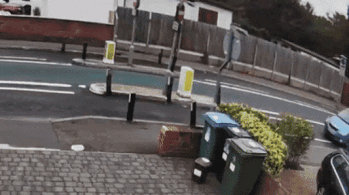 a blue car is driving down a street next to a fence
