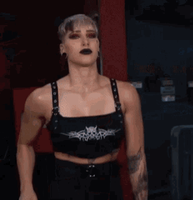 a woman wearing a black crop top with a skull on it is standing in a dark room .
