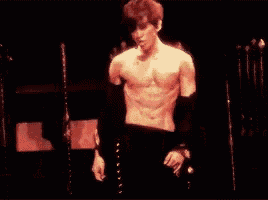 a man without a shirt is singing into a microphone on stage .