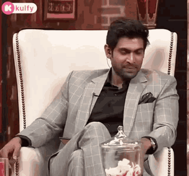 a man in a suit is sitting in a chair with his legs crossed and a jar of popcorn in his hand .