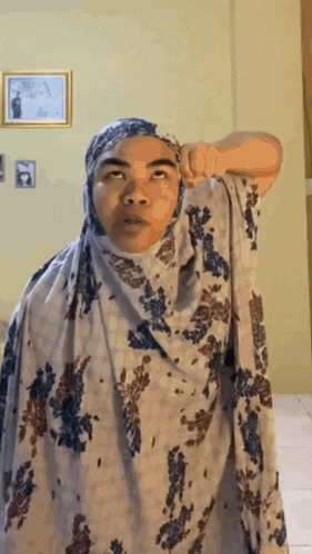 a woman wearing a hijab is standing in a room with her hands on her head .