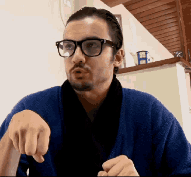 a man wearing glasses and a blue robe points his finger