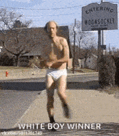a shirtless man in underwear is running down a sidewalk in front of a sign that says entering woonsocket .