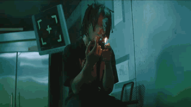 a man is lighting a cigarette in front of a monitor that has the letter l + on it