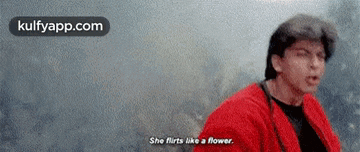 a man in a red jacket is talking to a woman and says she flirts like a flower .