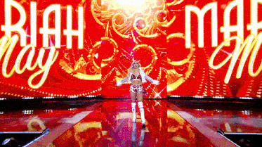 a woman stands on a stage in front of a large screen that says ' riah may '