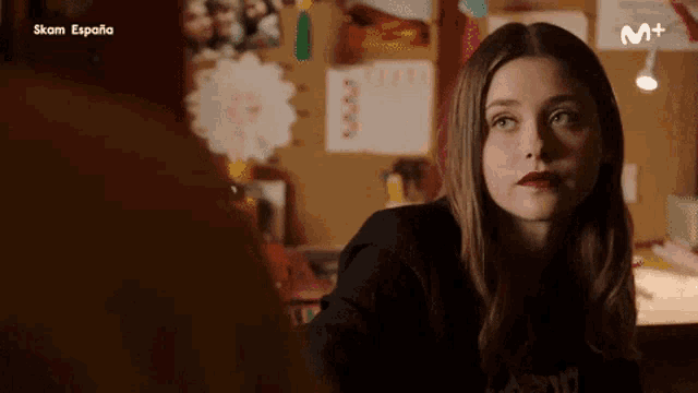 a woman is sitting at a desk in front of a bulletin board with spanish writing on it