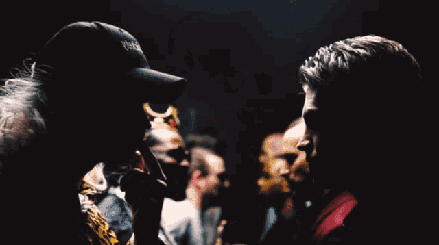 a man wearing a hat that says ' yeezy ' on it stands next to another man