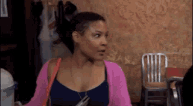 a woman wearing a pink cardigan and a blue tank top is standing in a room .