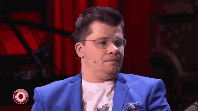 a man wearing glasses and a blue suit has a microphone on his neck