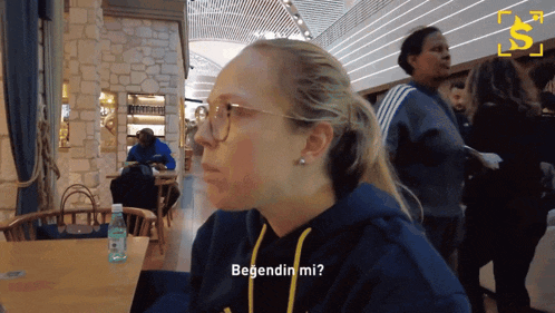 a woman wearing glasses is sitting at a table and says " begendin mi " in a foreign language