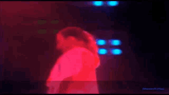 a blurry picture of a person in a red shirt on a stage with blue lights behind them