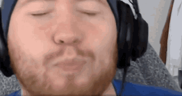 a man with a beard is wearing headphones and making a funny face with his eyes closed .