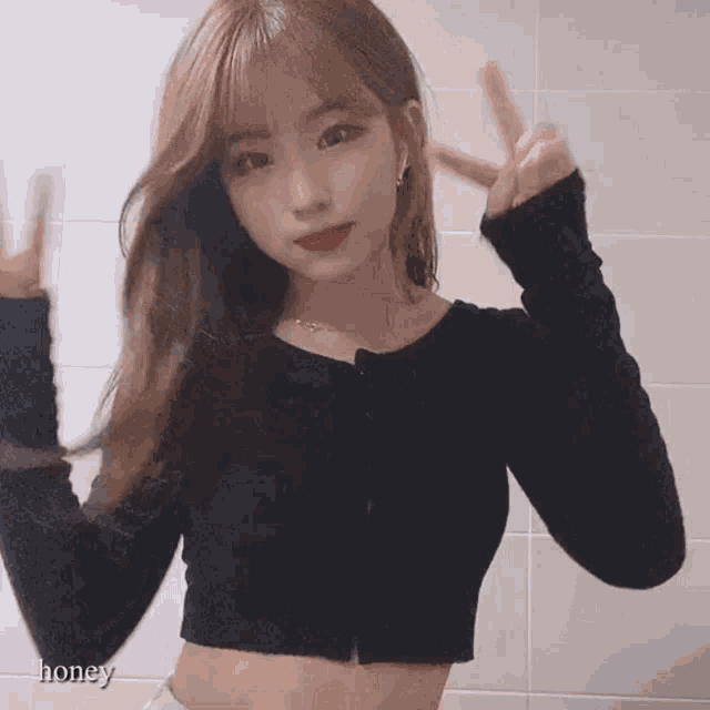 a girl in a black crop top is giving a peace sign .