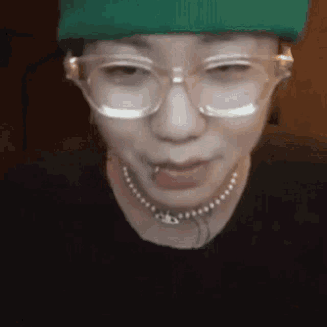 a close up of a person wearing glasses , a necklace , and a green hat .