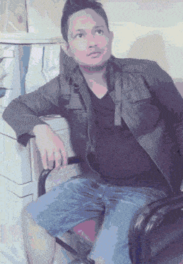 a man wearing a black shirt and a leather jacket sits in a chair