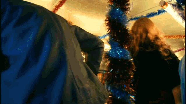 a woman in a black dress stands in front of a christmas tree decorated with blue and gold tinsel