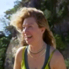a woman wearing a yellow tank top and a pearl necklace smiles