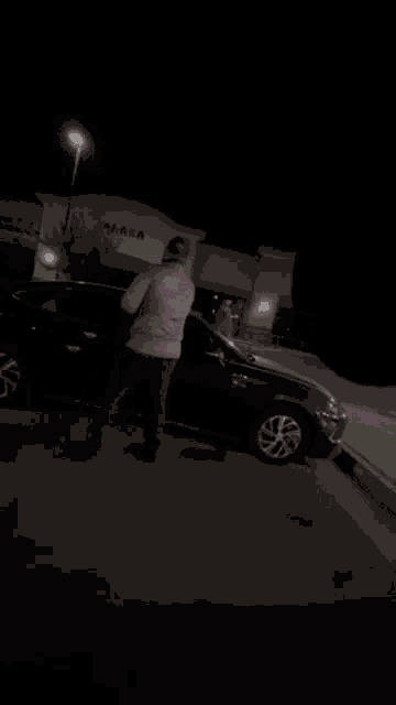 a man is opening the door of a black car in a parking lot
