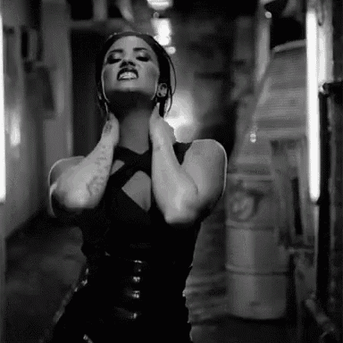 a black and white photo of a woman in a black dress standing in a hallway with her hands on her neck .