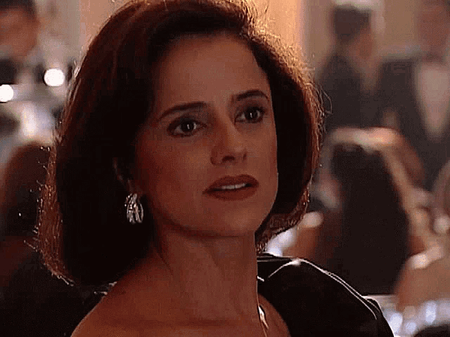 a woman in a black dress and earrings is looking at the camera with a surprised look on her face .