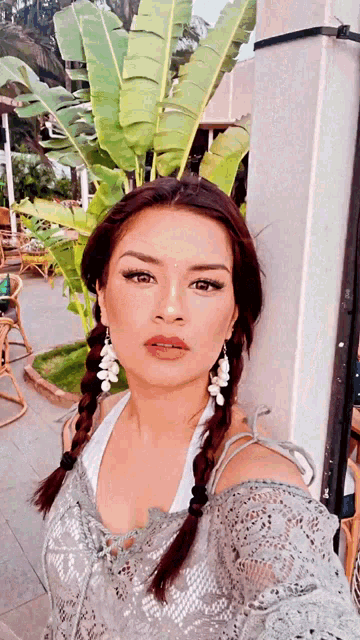 a woman wearing braids and earrings takes a selfie in front of a palm tree