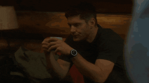 a man wearing a watch is sitting on a couch and looking at his phone