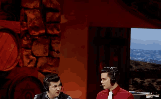 a man in a red shirt and white tie talks to another man