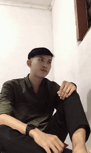 a young man wearing a watch sits in a corner of a room