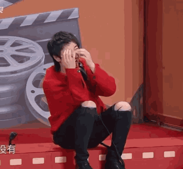 a man in a red jacket is covering his face with his hands while sitting on a red step