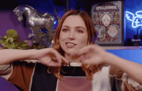a woman making a heart shape with her hands in front of a spelljammer sign